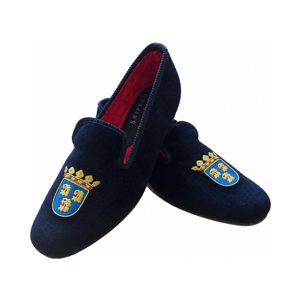The Albert slipper in black velvet, three gold lions' heads on a blue shield beneath a coronet embroidered on the vamp, red quilted lining.