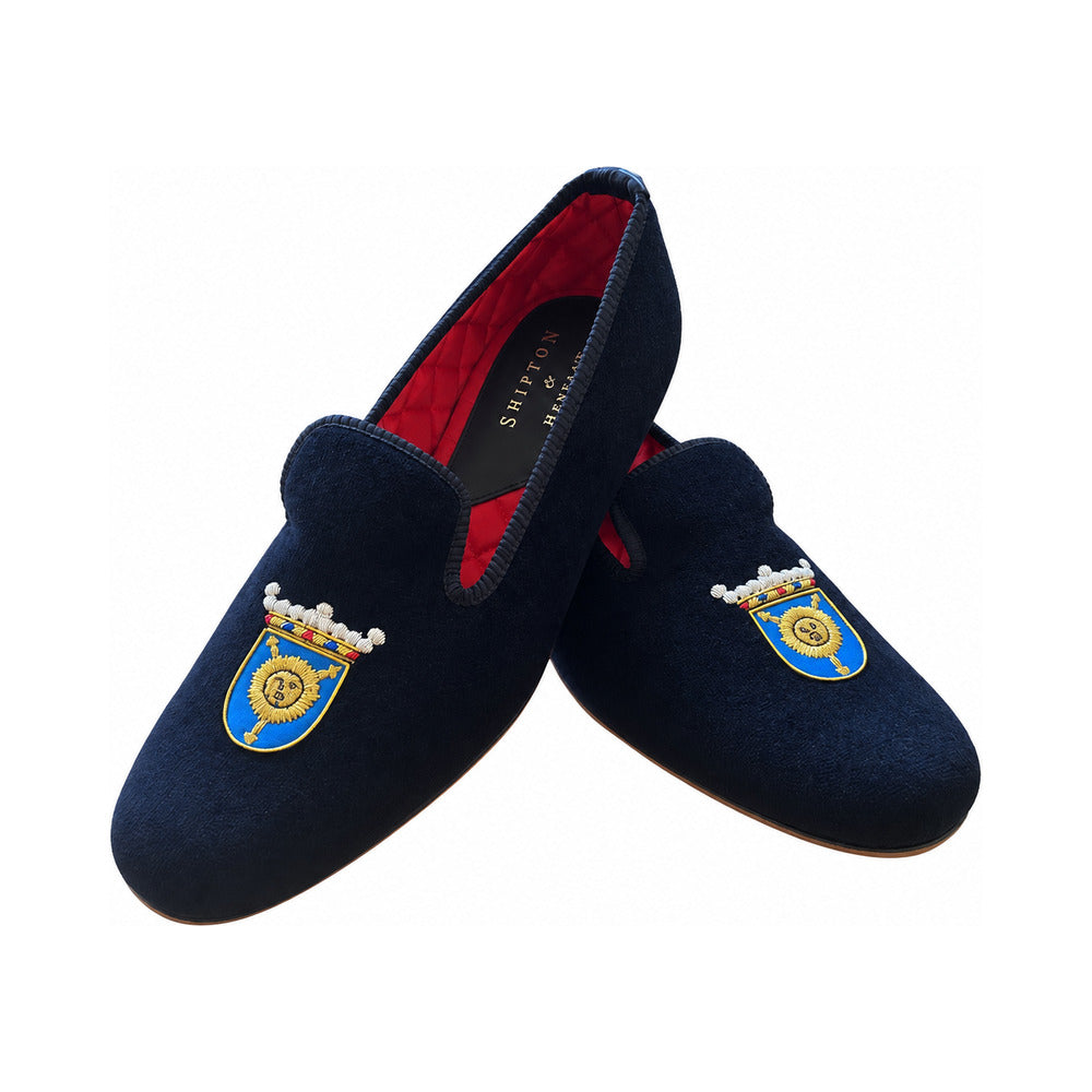 The Albert slipper in black velvet, a golden sun on a blue shield beneath a plumed coronet embroidered on the vamp, red quilted lining.